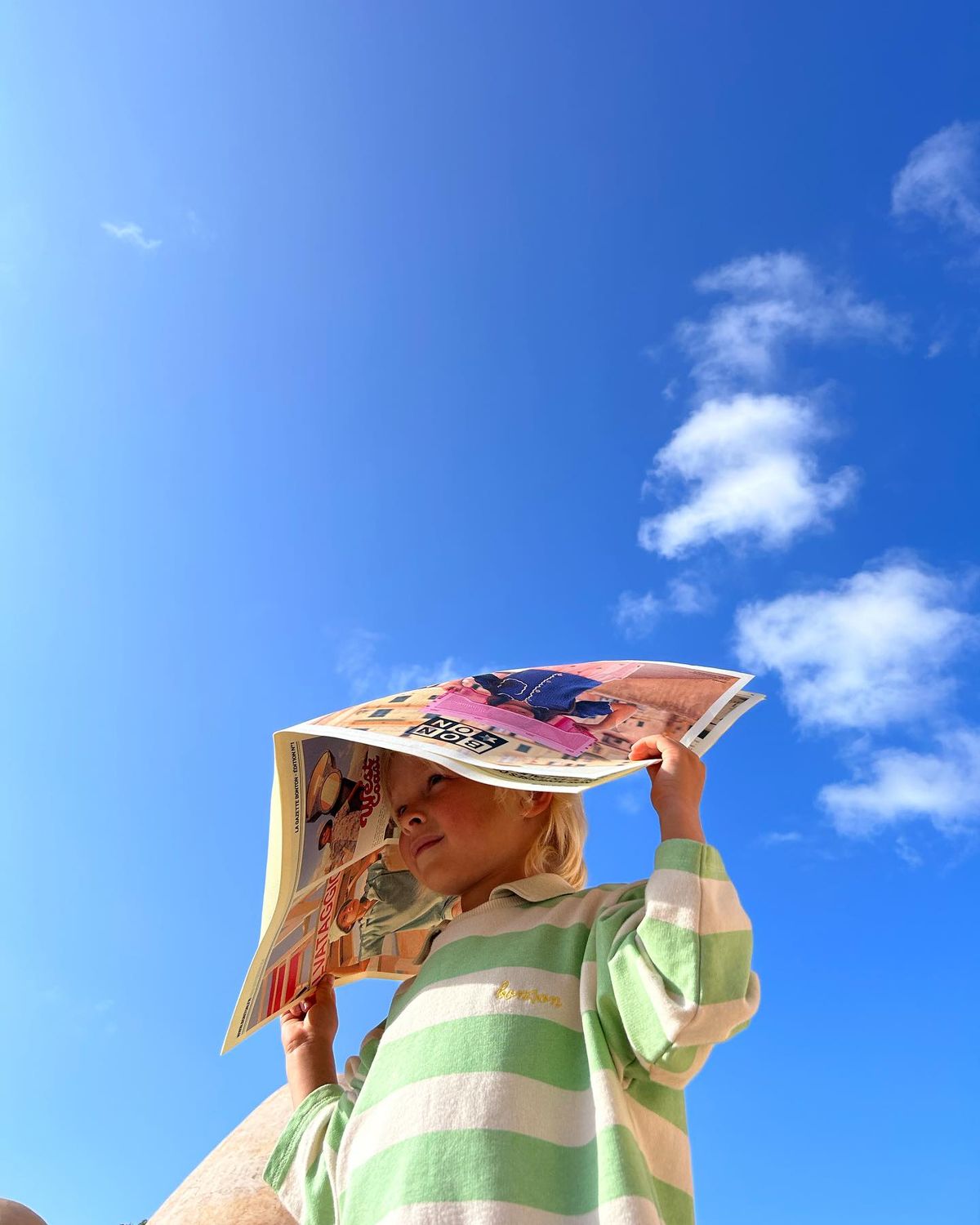 Bambina che si ripara dal sole con un giornale sotto il cielo azzurro